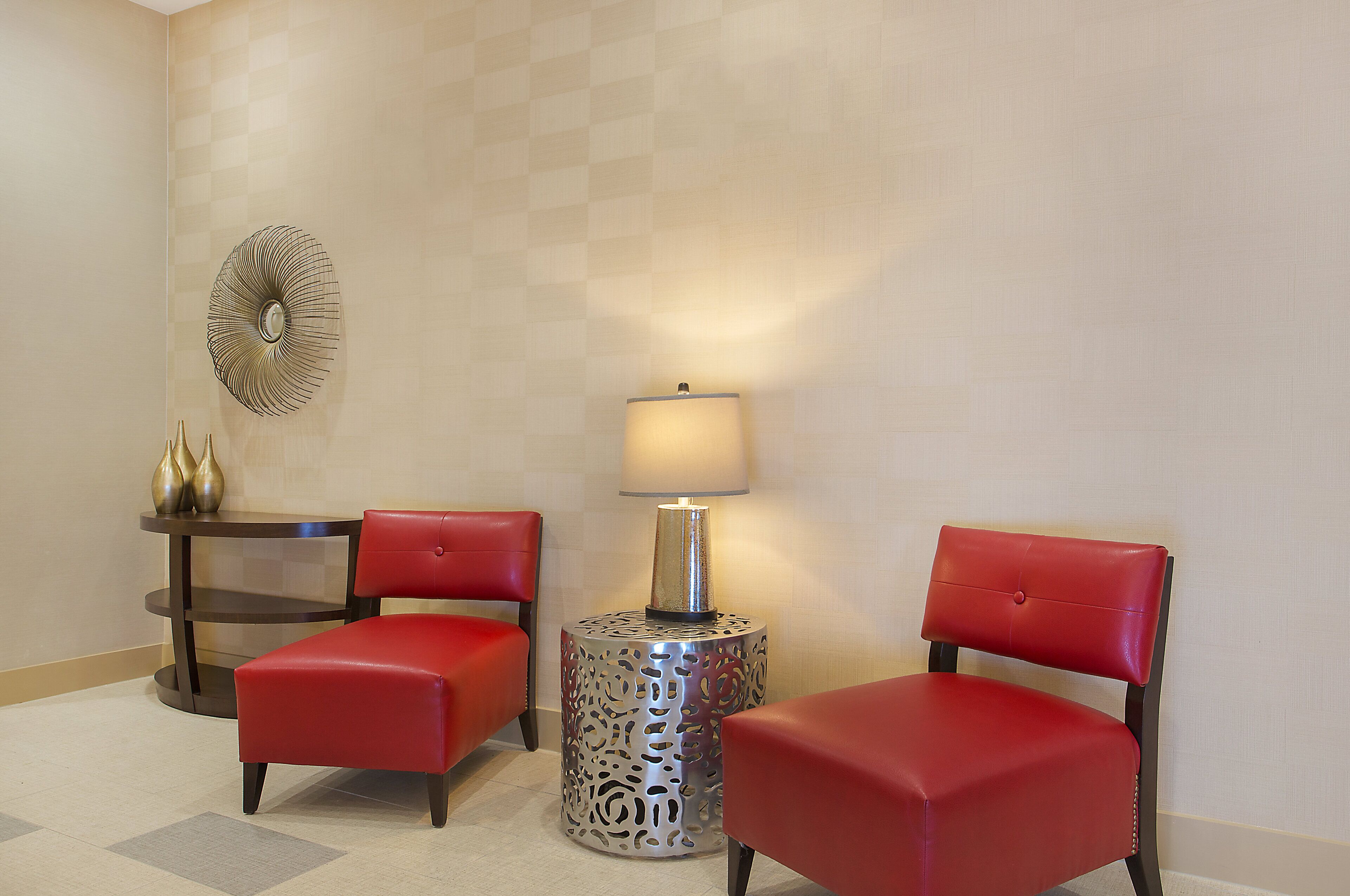 A room with two red leather chairs, a small round table with a lamp, and a decorative wall piece.