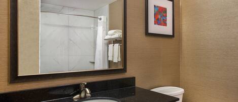 A bathroom with a large mirror, a sink, a toilet, and a framed abstract painting on the wall.