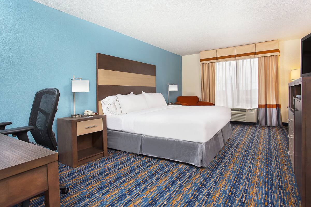 A hotel room with a bed, desk, chair, and a television.