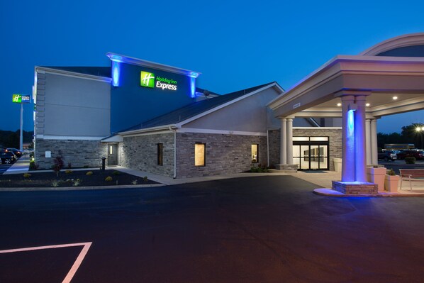A Holiday Inn Express building with a stone facade, a well-lit entrance, and a gas station with a blue-lit canopy.