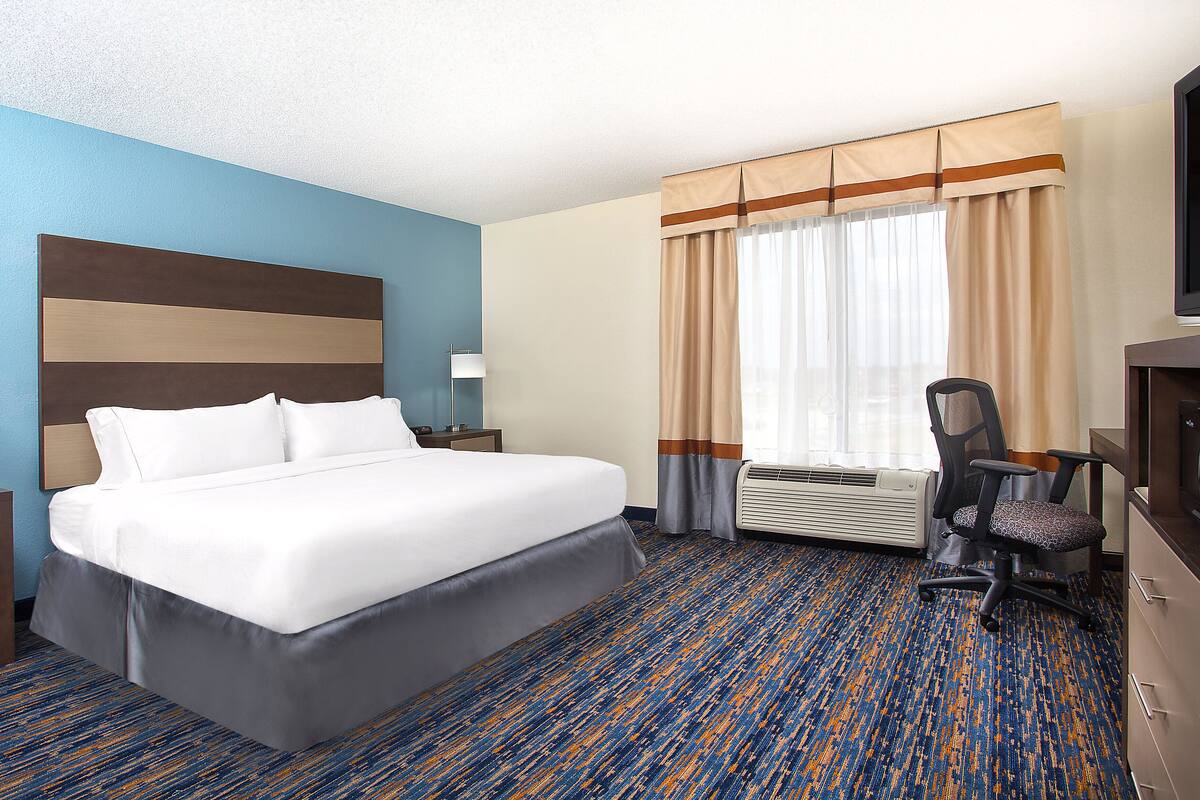 A hotel room with a large bed, a desk, a chair, and a TV.