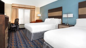 A hotel room with two beds, a desk, a chair, a lamp, and a large window with curtains.