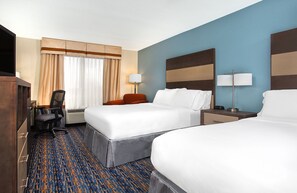 A hotel room with two beds, a desk, a chair, a lamp, and a large window with curtains.