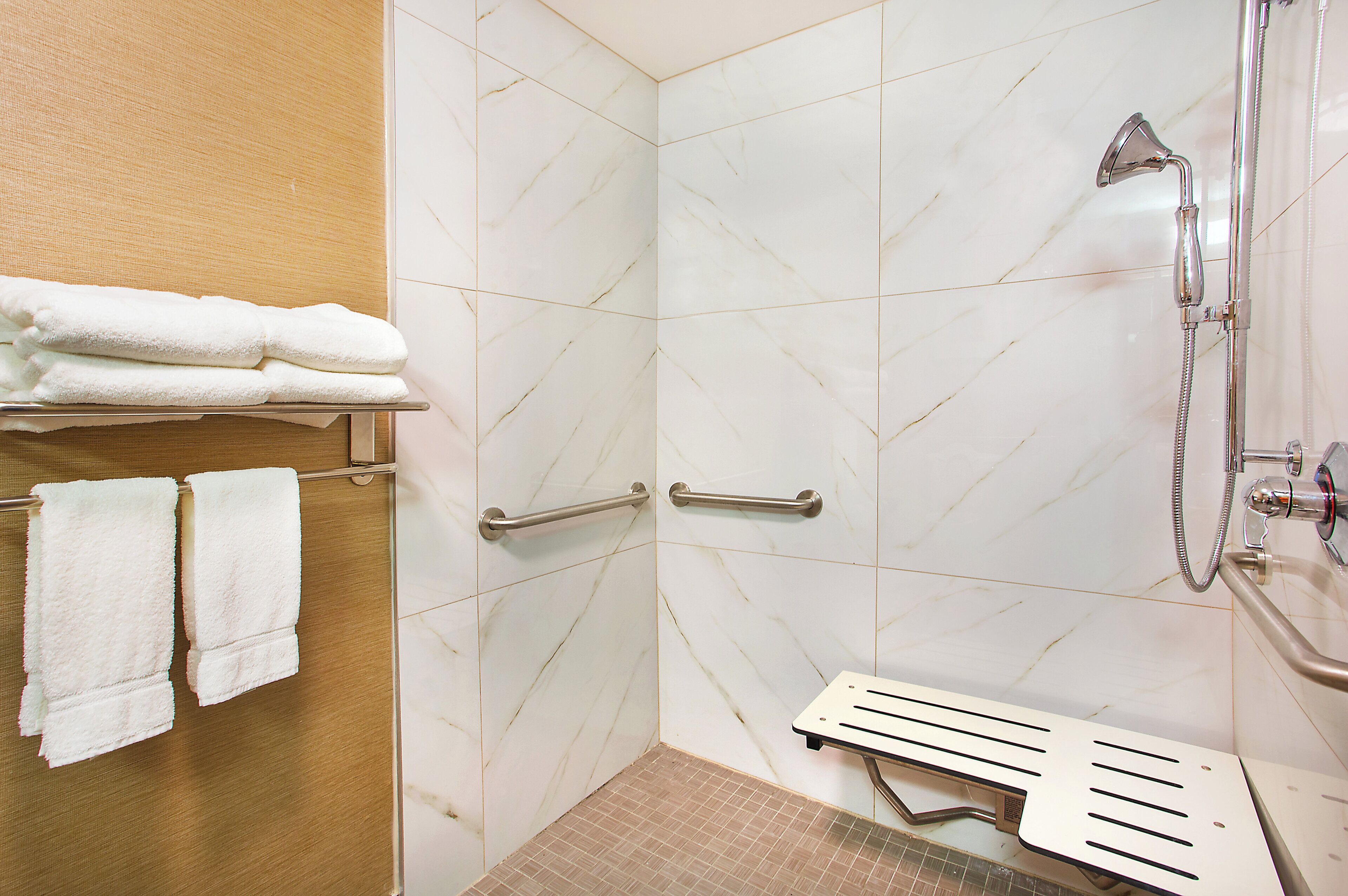 Une salle de bain carrelée de marbre blanc, une douche avec un pommeau de douche amovible et un porte-serviettes avec des serviettes pliées.
