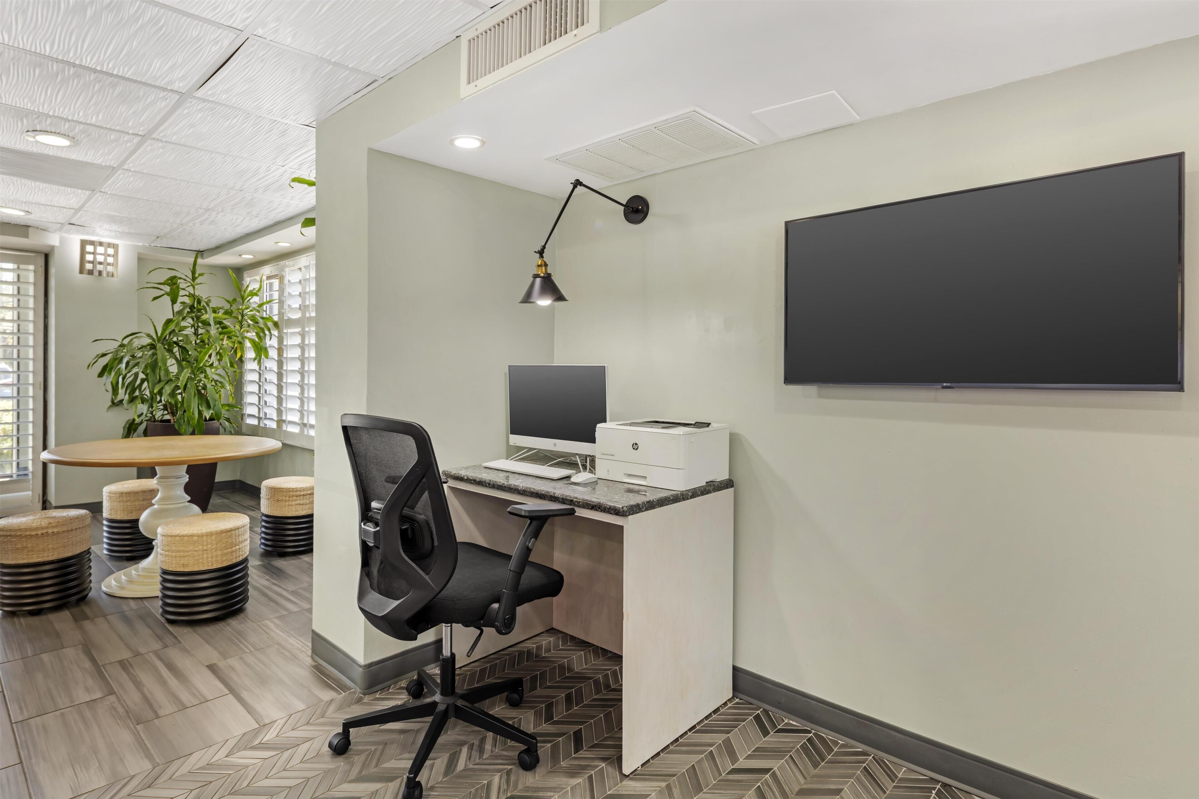 A modern office with a desk, chair, computer, printer, and a large flat-screen TV mounted on the wall.