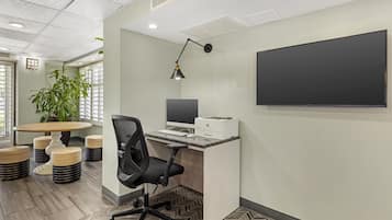 A modern office with a desk, chair, computer, printer, and a large flat-screen TV mounted on the wall.