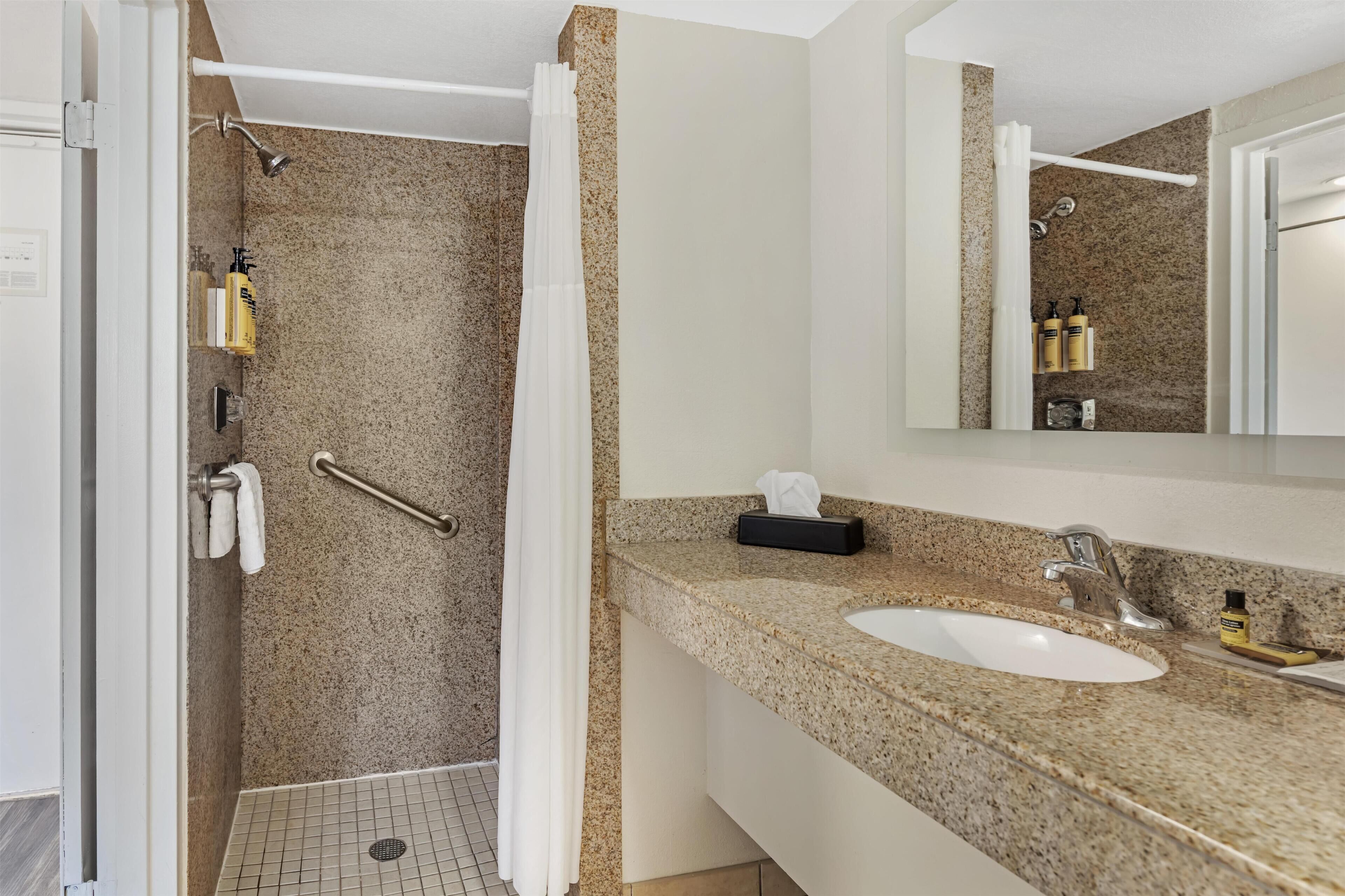 A bathroom with a shower, a sink, a mirror, and toiletries.