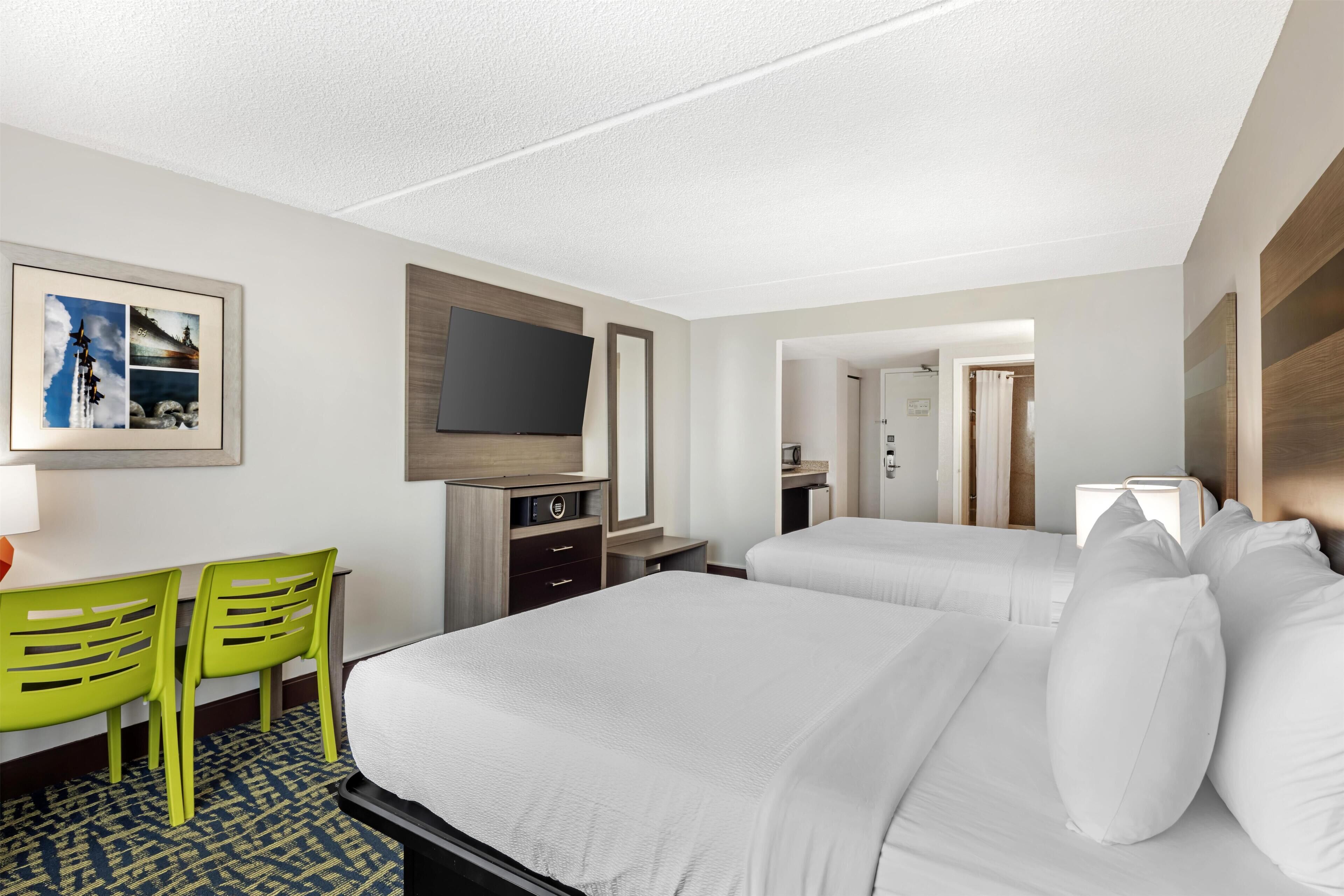 Una habitación de hotel con una cama, un escritorio con silla, un televisor y un cuadro en la pared.