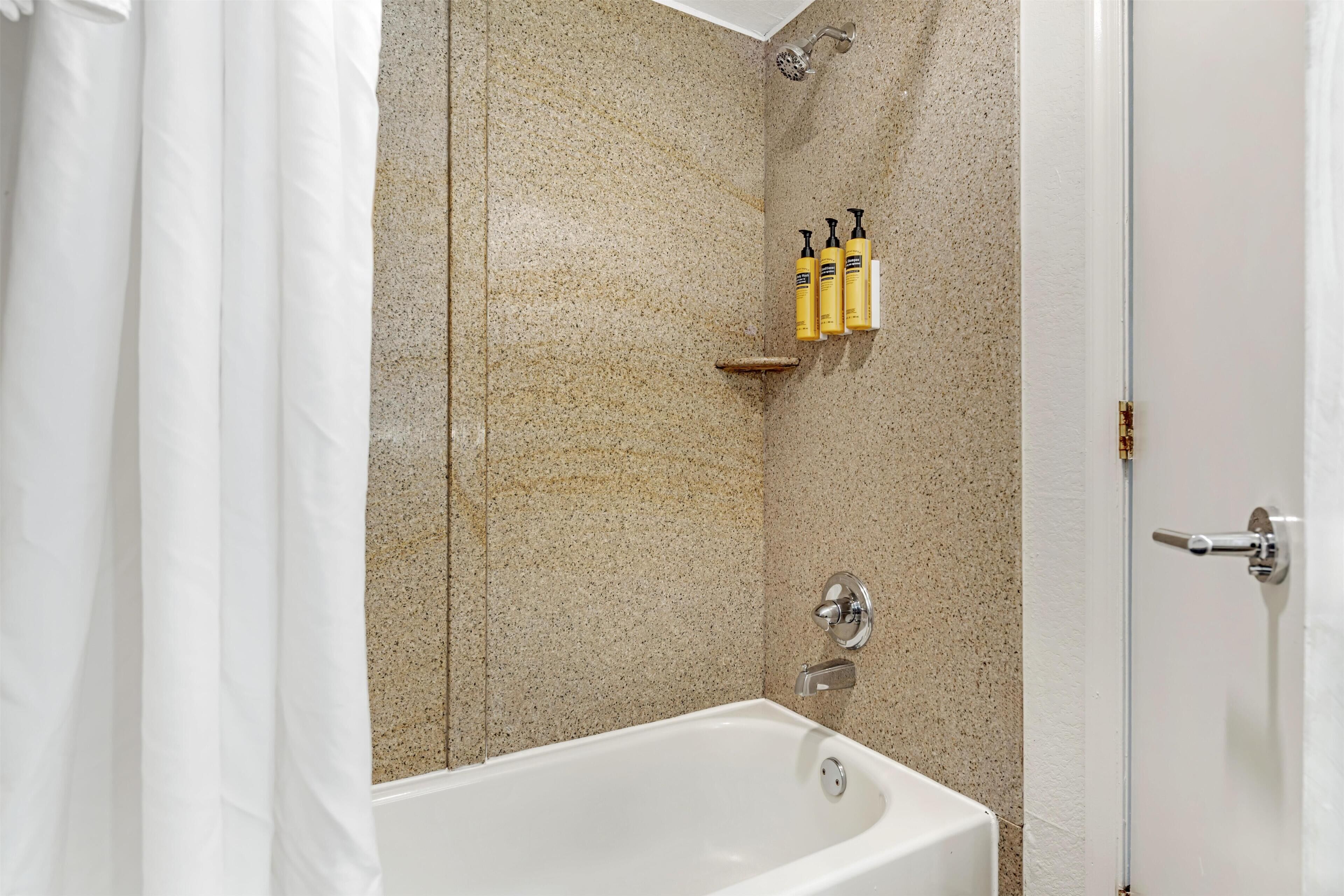 A bathroom with a bathtub, shower, and a shelf with toiletries.