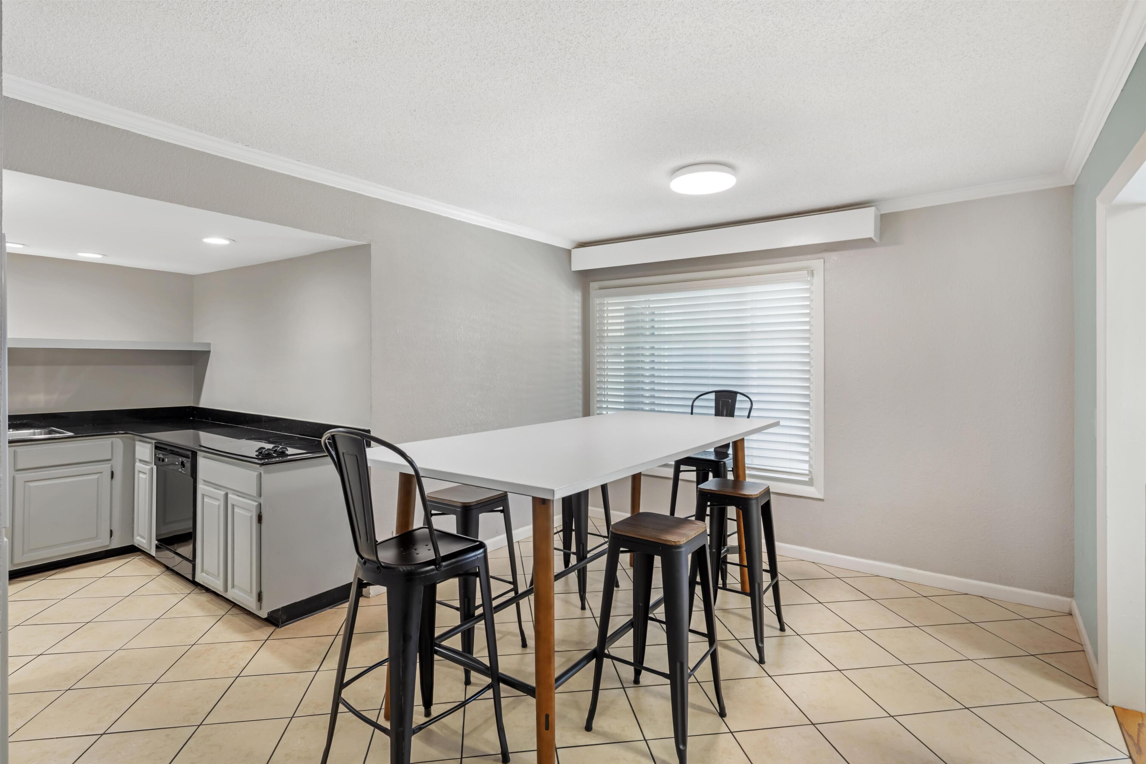 A kitchen with a white table and four stools, a built-in oven, and a window with blinds.