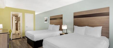 A hotel room with two beds, a desk, and a bathroom visible through an open door.