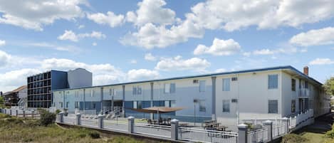 Un bâtiment moderne doté d’un toit plat, de nombreuses fenêtres et d’un espace extérieur abrité avec des tables et des chaises.