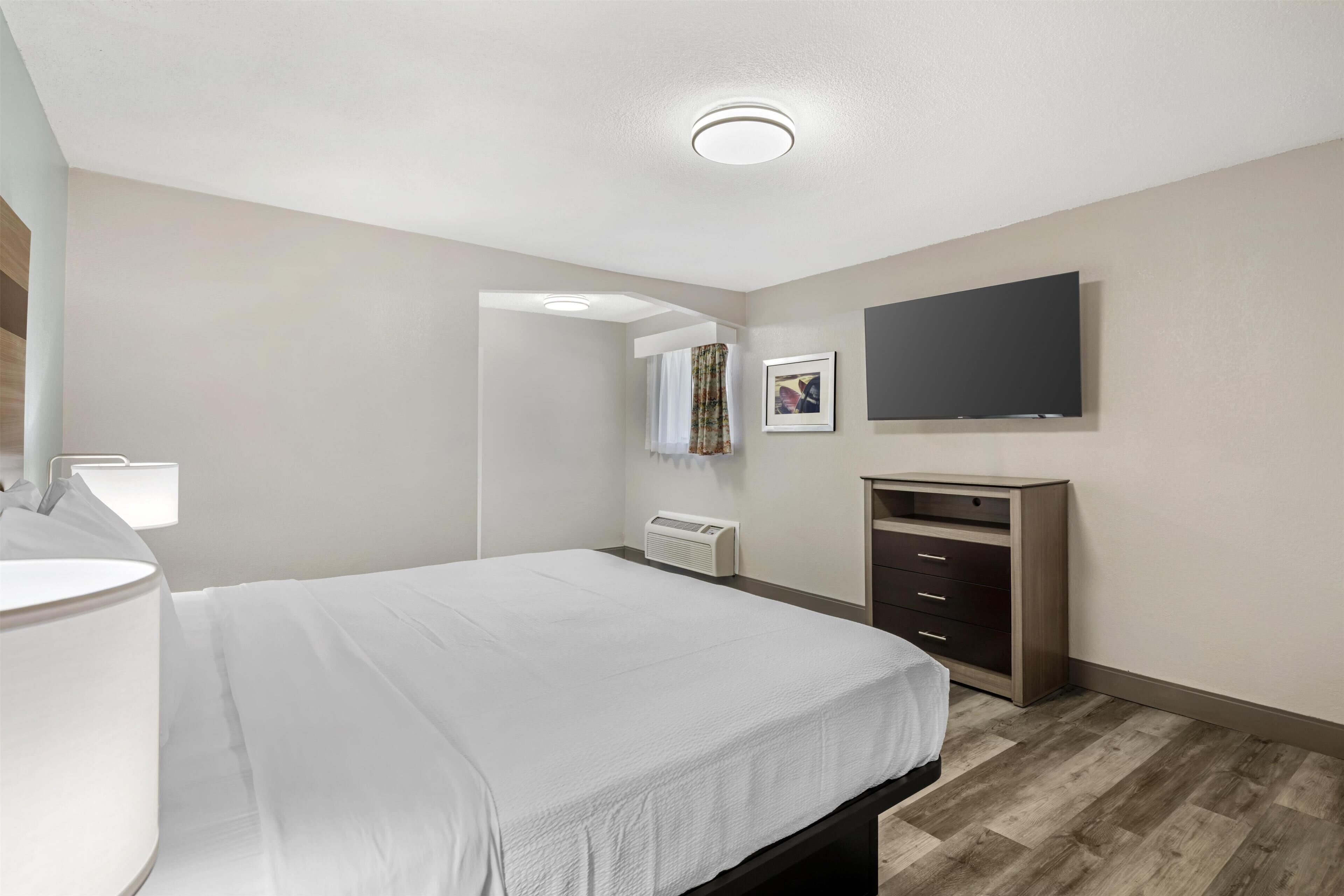 A hotel room with a bed, bedside lamp, TV, and a dresser.