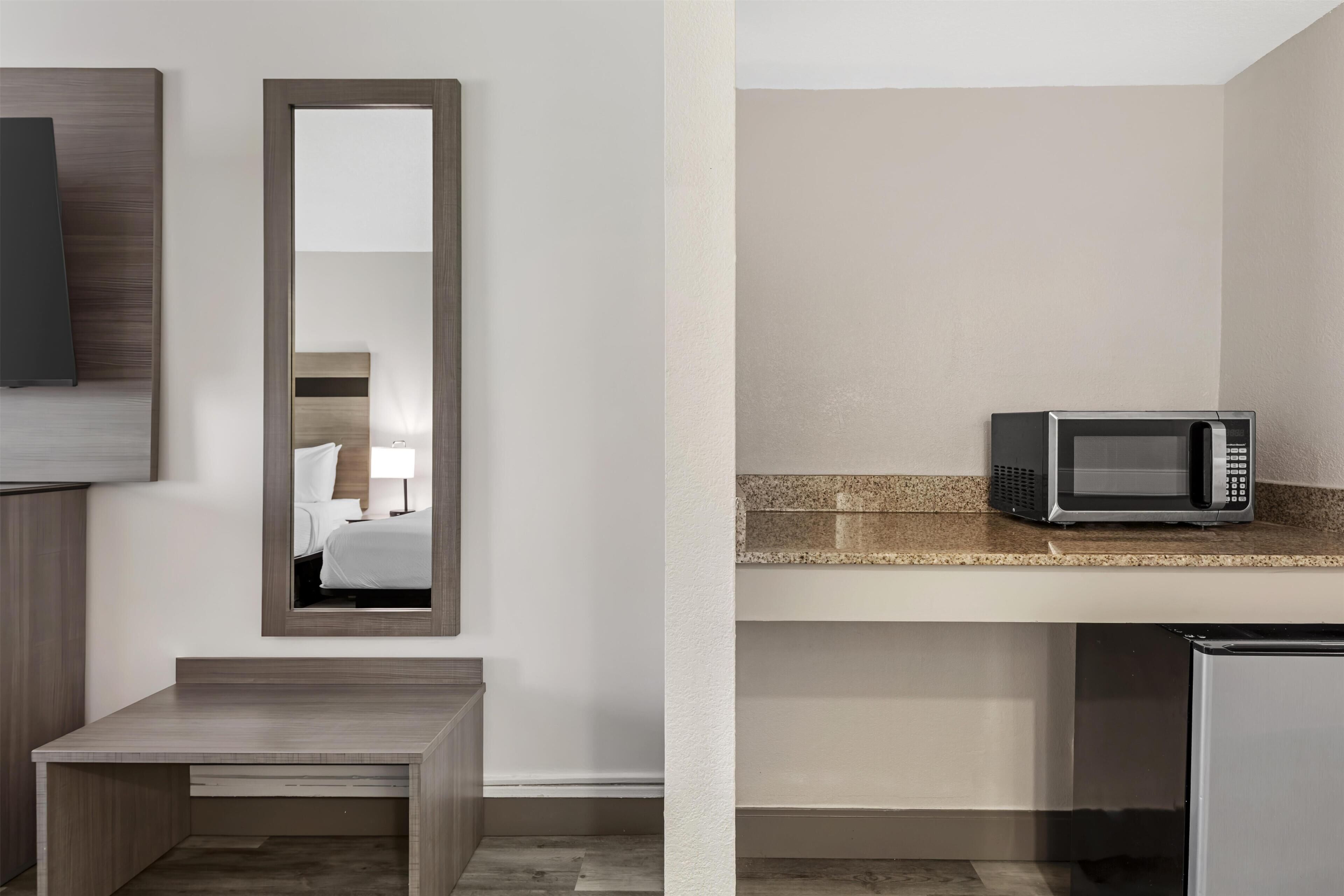 Une chambre d’hôtel avec un bureau en bois, un miroir, un four à micro-ondes et un petit placard.