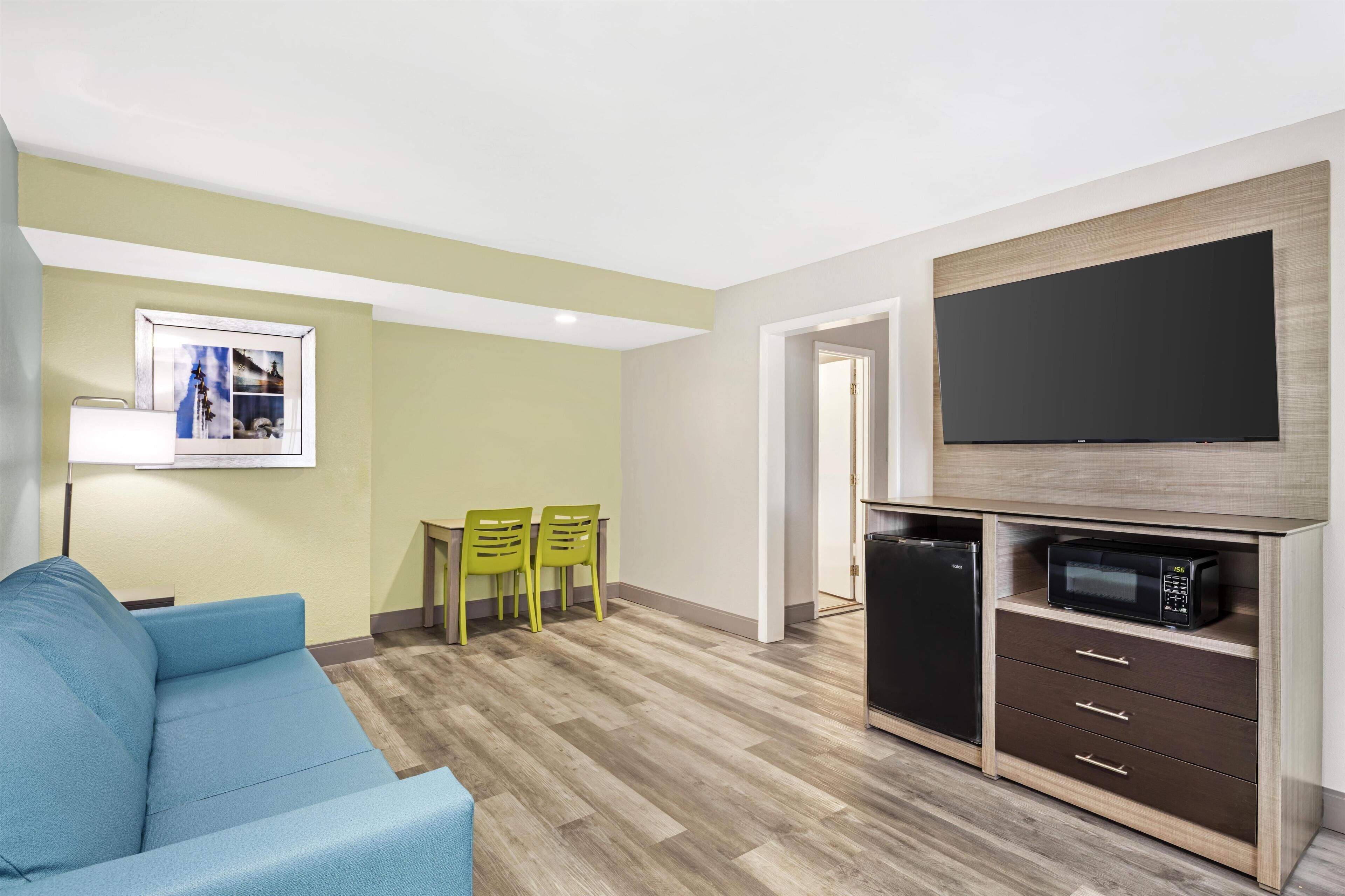 A compact living space with a sofa, a dining table with chairs, a flat-screen TV, a microwave, and a refrigerator.