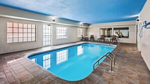 An indoor swimming pool with clear blue water, tiled floor, and large windows allowing natural light.