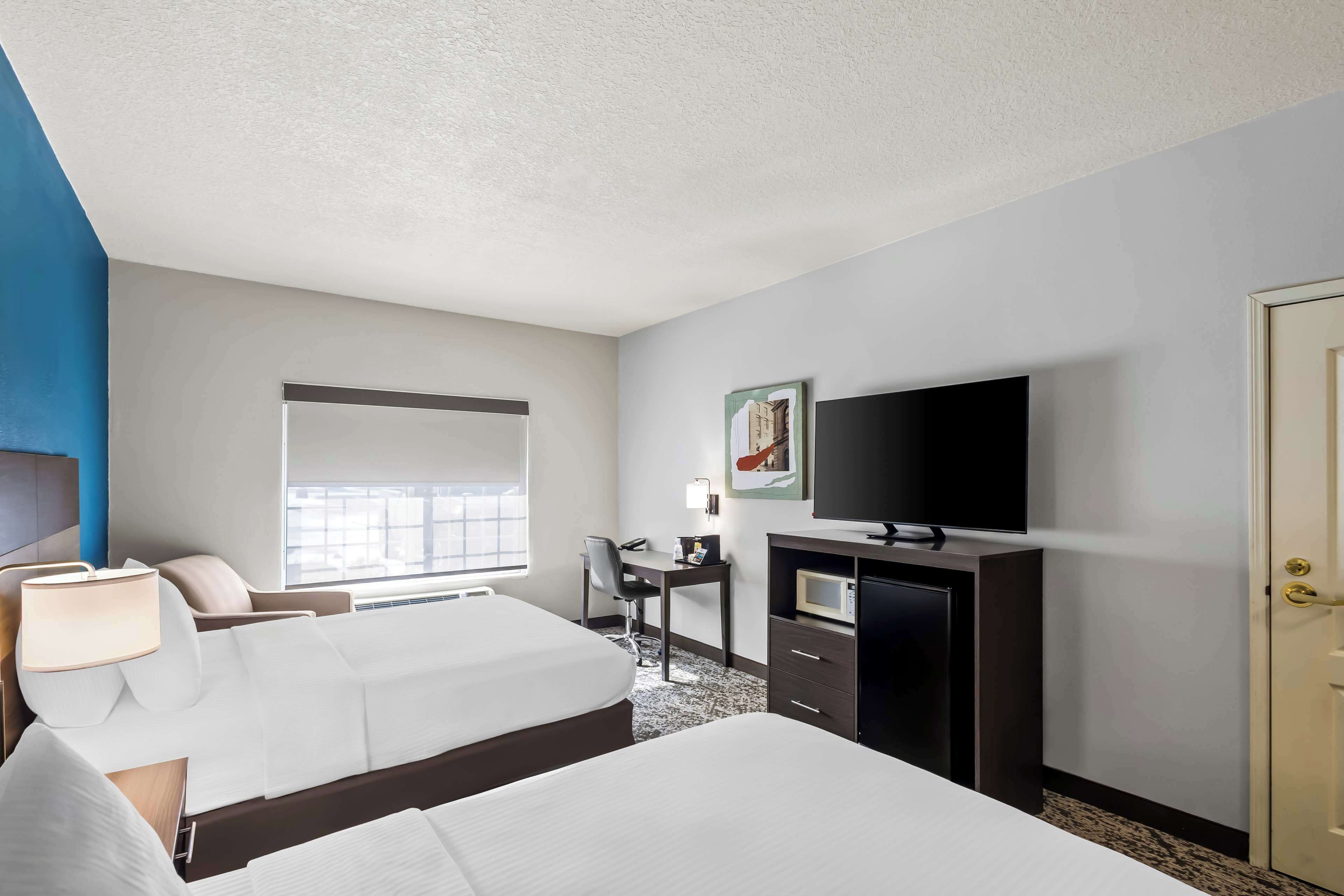 A hotel room with two beds, a desk, a television, and a door.