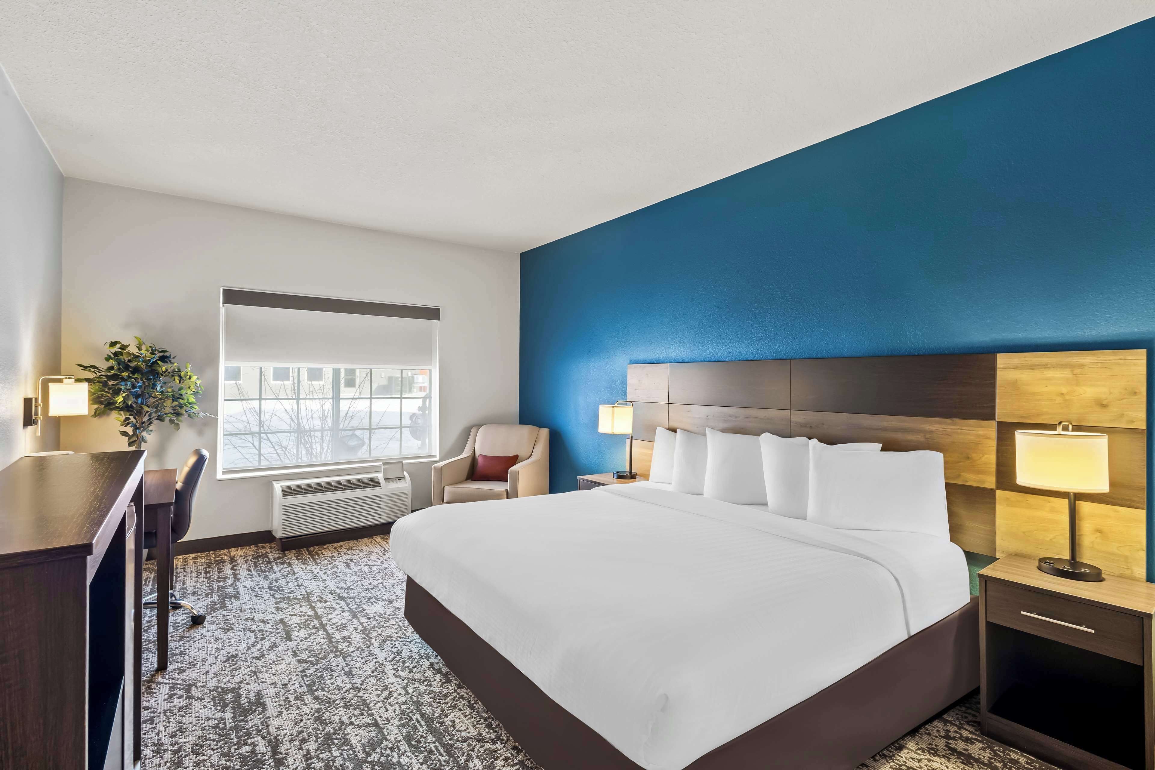 Ein Hotelzimmer mit einem großen Bett, einem Schreibtisch, einem Stuhl, einem Nachttisch und einem Fenster.