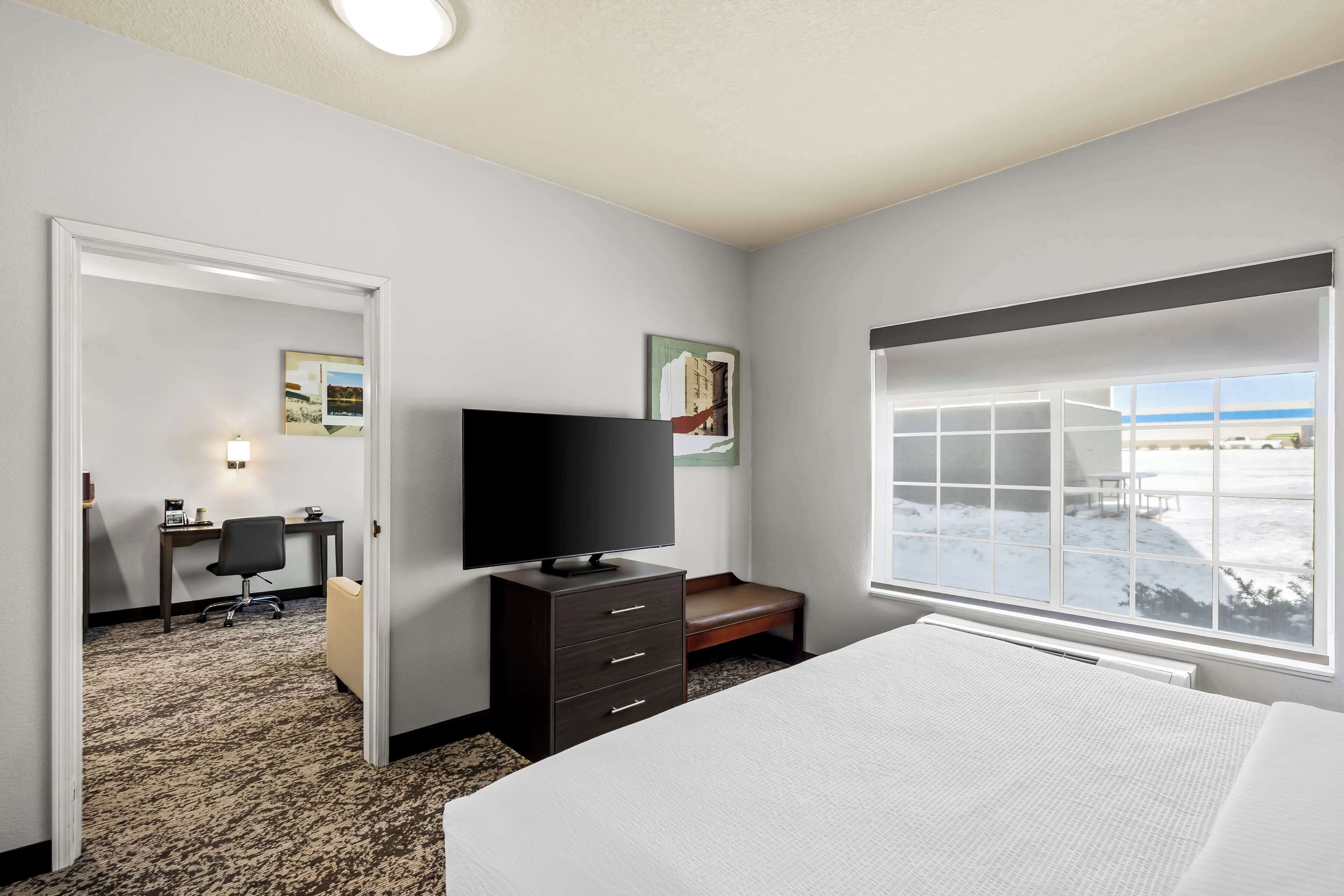 Quarto de hotel com cama, secretária com computador, televisão, janela com vista para uma paisagem nevada e porta que dá para outro quarto.