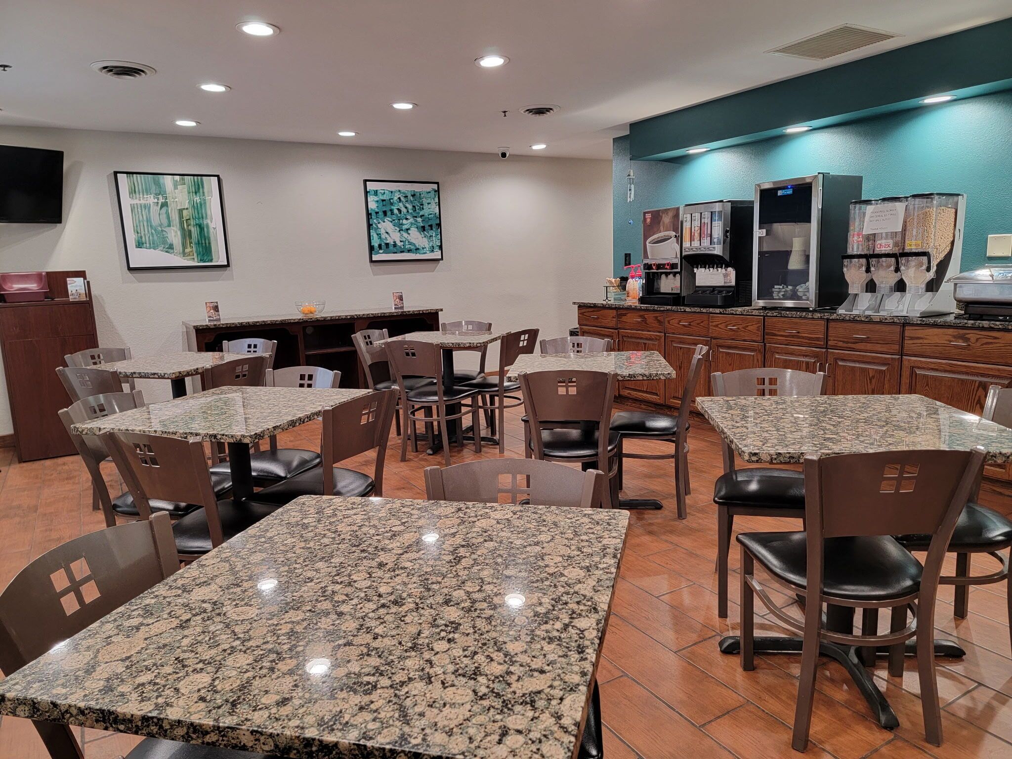 A restaurant with granite tables and chairs, a counter with coffee machines, and artwork on the walls.