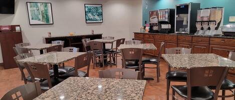 A restaurant with granite tables and chairs, a counter with coffee machines, and artwork on the walls.