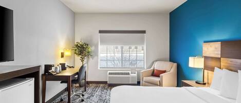 A hotel room with a bed, desk, chair, and a television.