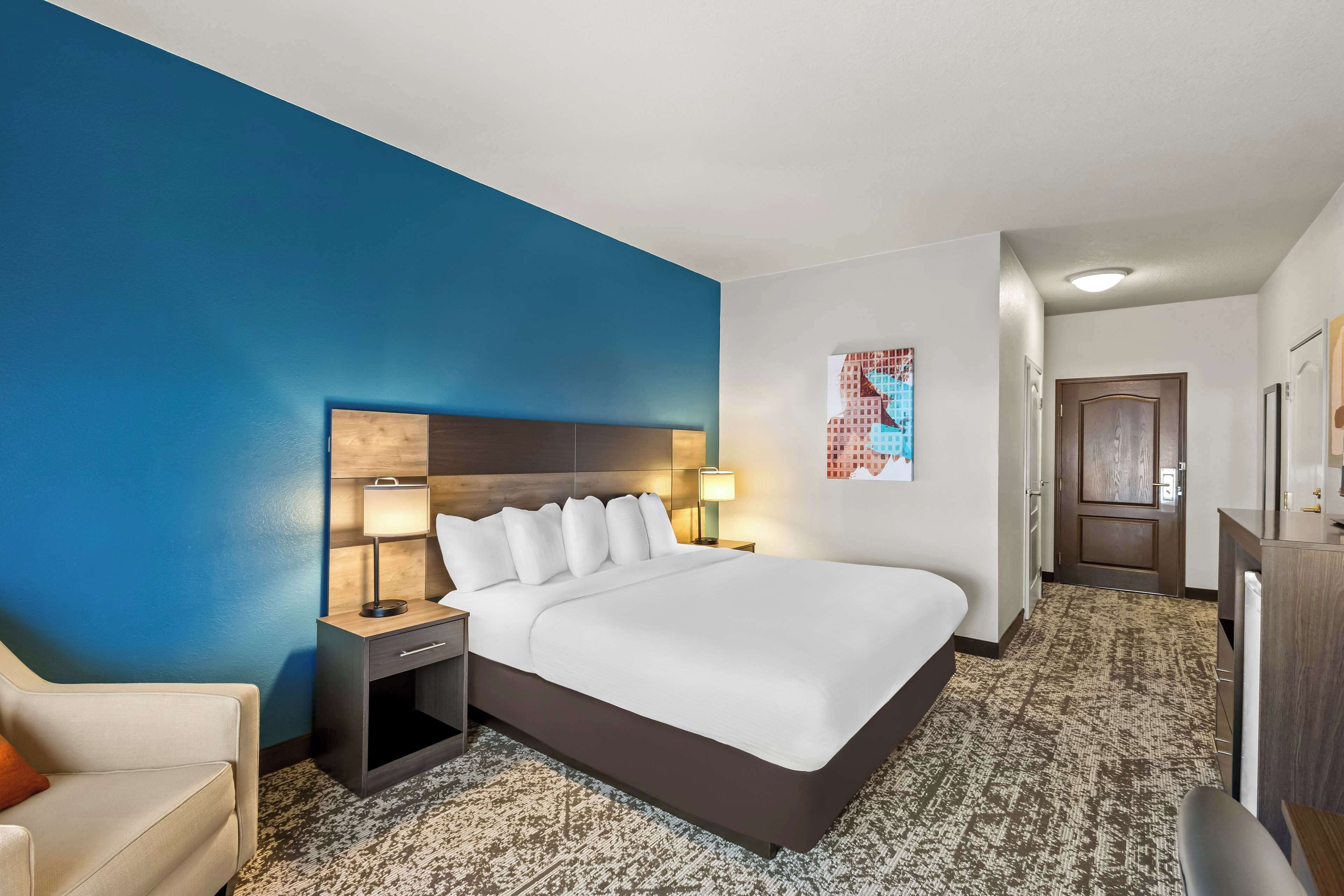 A hotel room with a large bed, a nightstand with a lamp, a chair, and a desk with a mirror.
