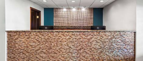 Una zona de recepción con pared de ladrillo, una puerta de madera y un computador Dell sobre el mostrador.