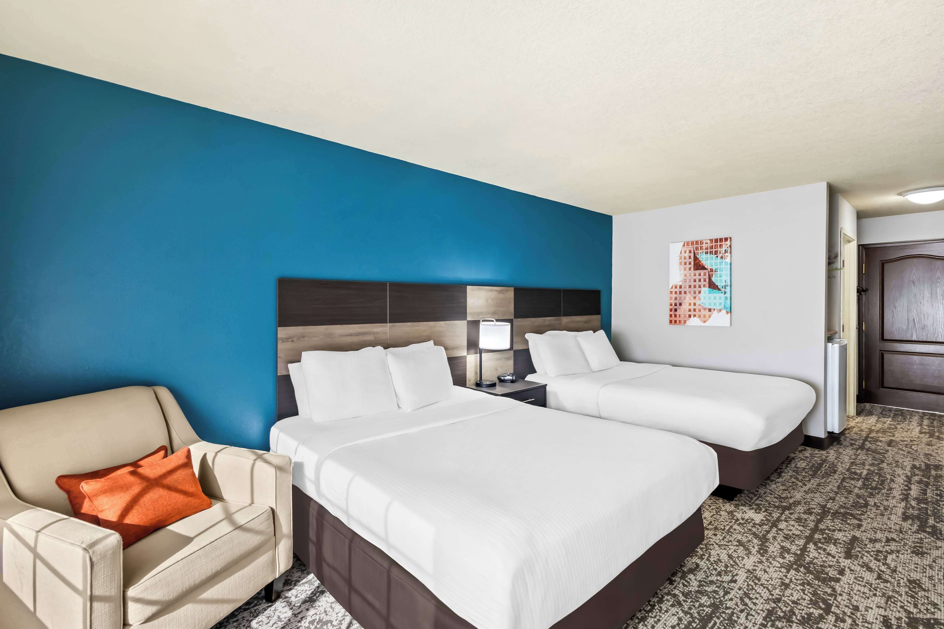A hotel room with two beds, a chair, a nightstand, and a wall art piece.