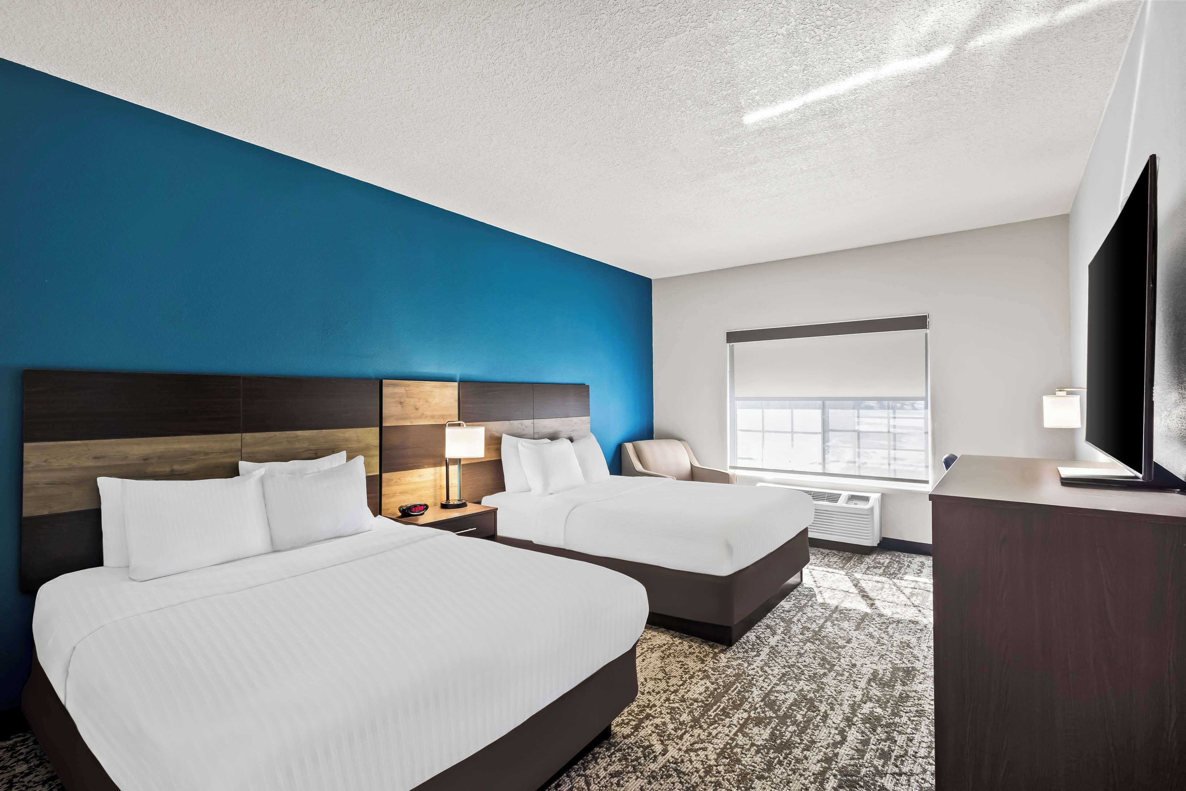 A hotel room with two beds, a TV, a desk, and a window with a view.