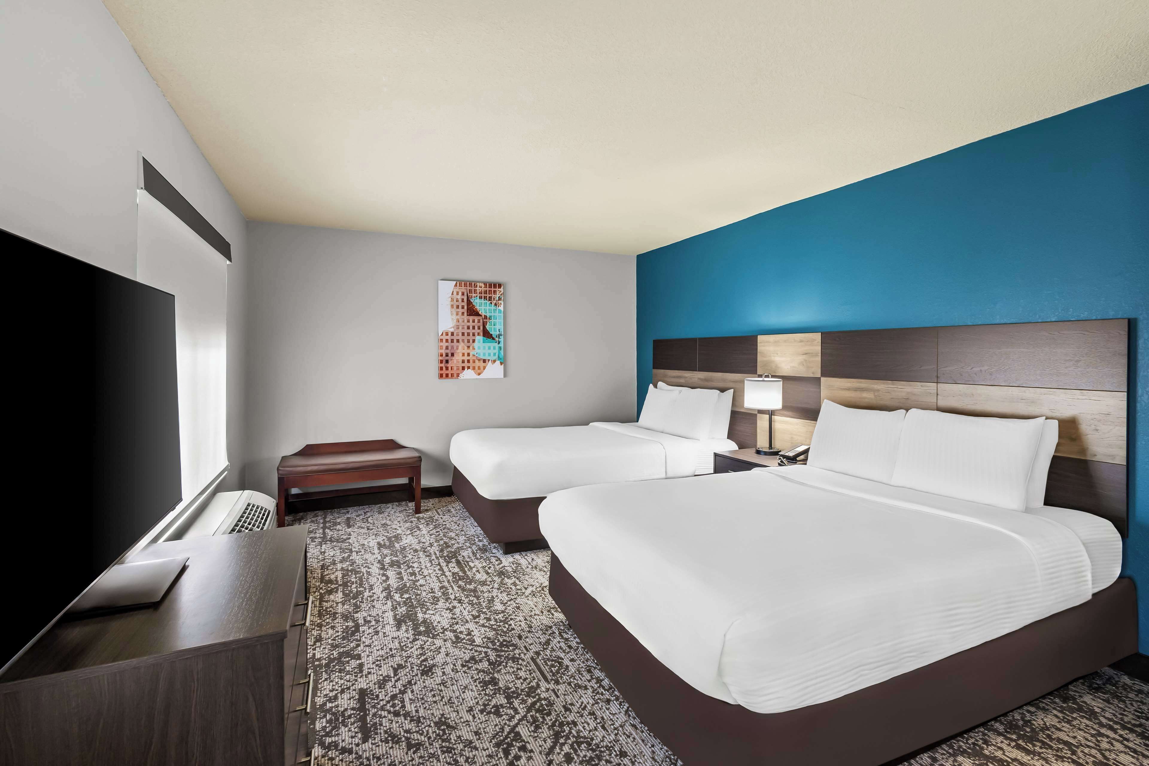 A hotel room with two beds, a flat-screen TV, a desk, a lamp, and a painting on the wall.