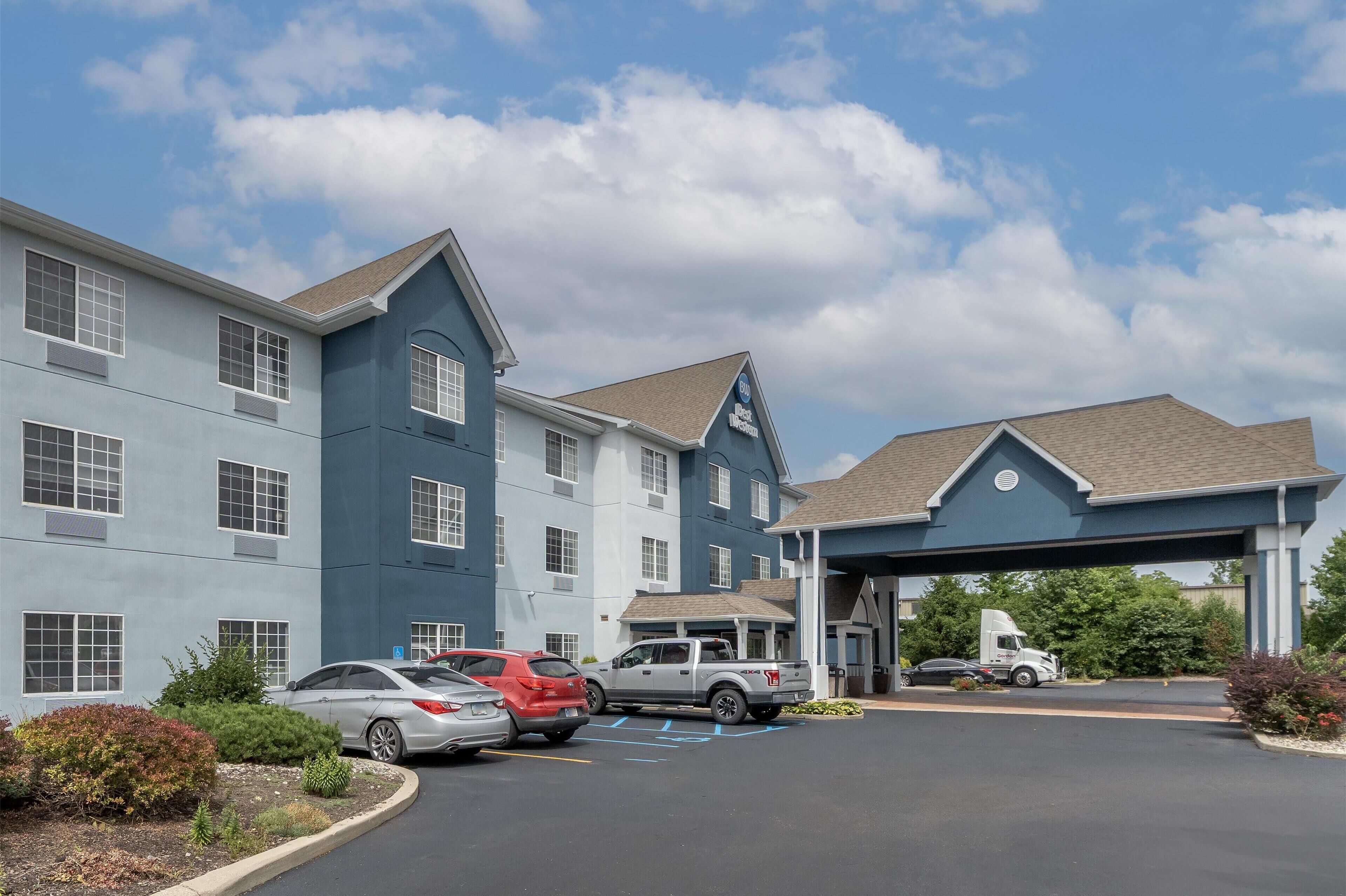 A hotel with a parking lot, a covered entrance, and a building with multiple windows and a blue facade.