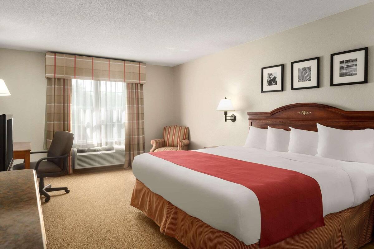 A hotel room with a large bed, a desk, a chair, a window with curtains, and three framed pictures on the wall.