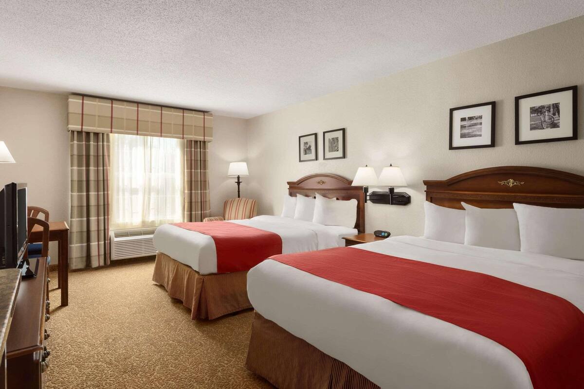 A hotel room with two beds, a desk, a chair, and a TV.