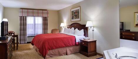 A hotel room with a bed, bedside table, lamp, TV, and a large bathroom with a bathtub.