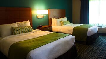 A hotel room with two beds, a nightstand, and a wall-mounted lamp.