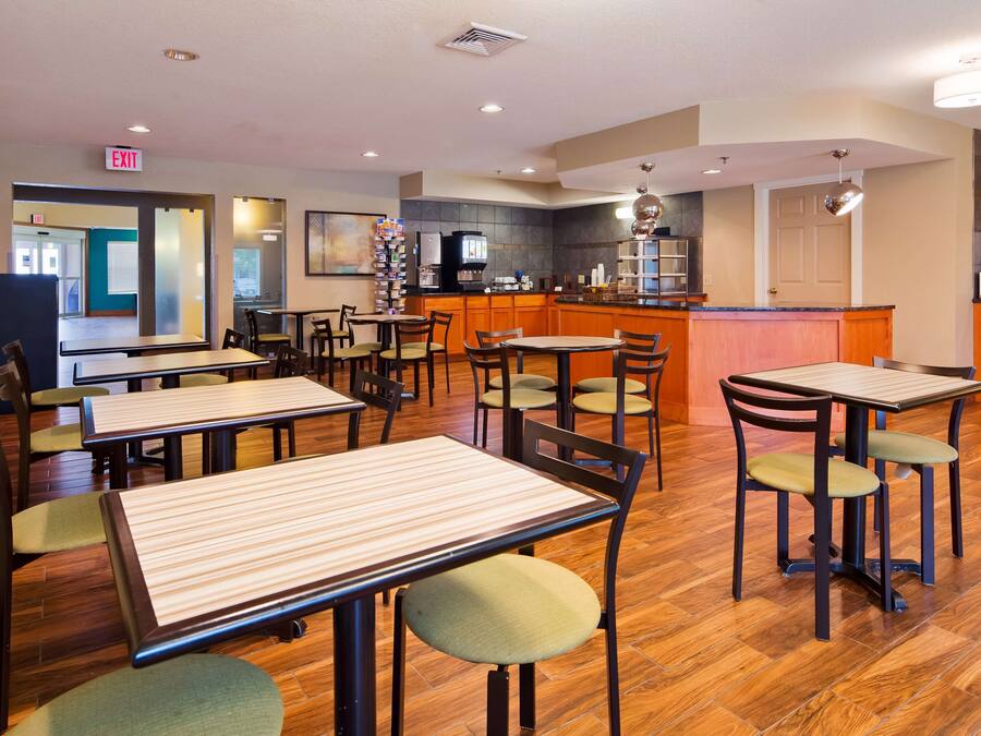A restaurant with wooden tables and chairs, a kitchen area, and an exit sign.