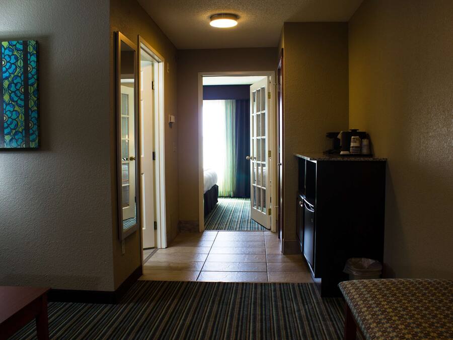 A hotel hallway with a carpeted floor, a bed in the background, and a television on a stand.
