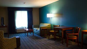 A hotel room with a sofa, armchair, dining table, and lamp.