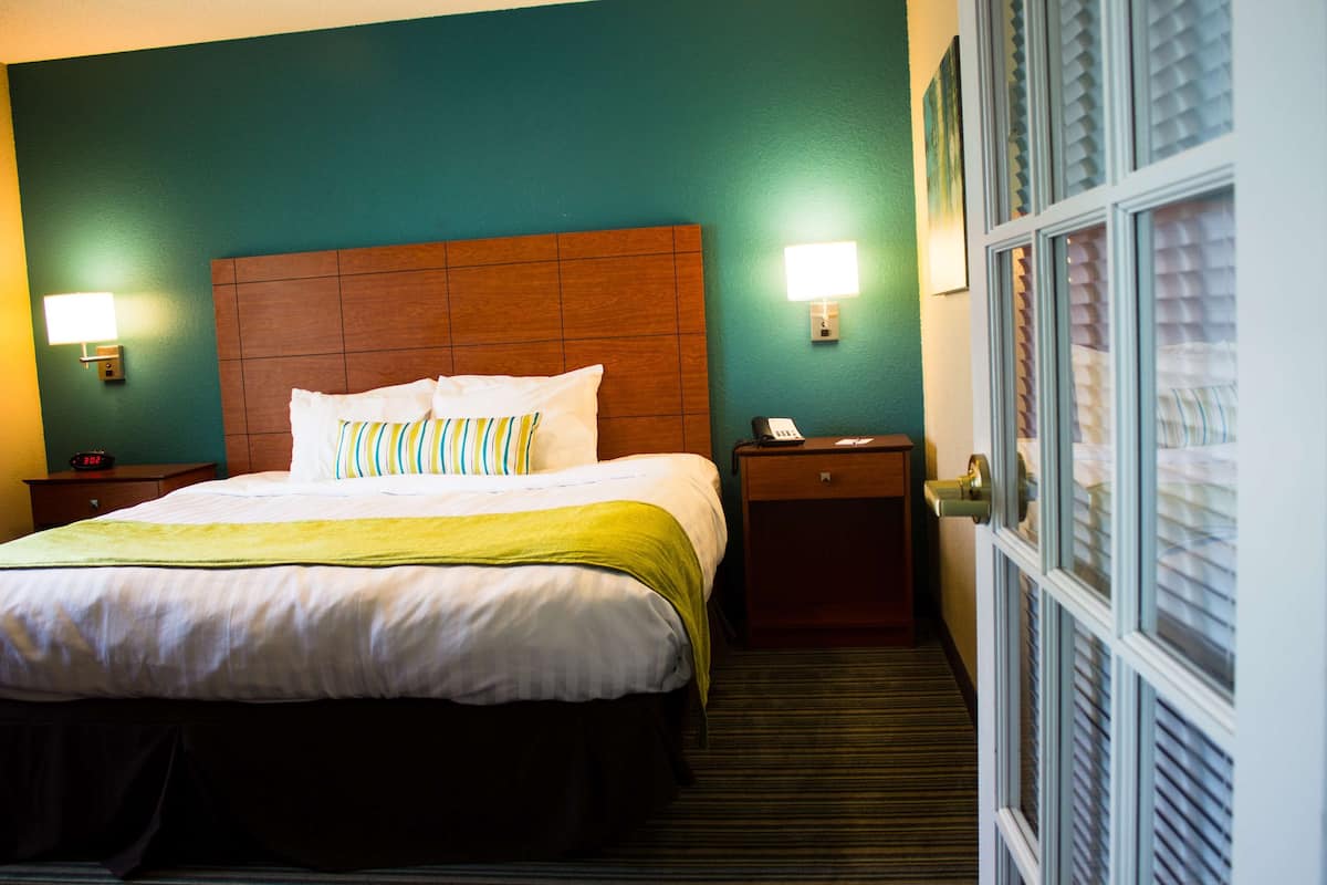 Una habitación de hotel con una cama grande, dos mesitas de noche y una puerta con persianas.