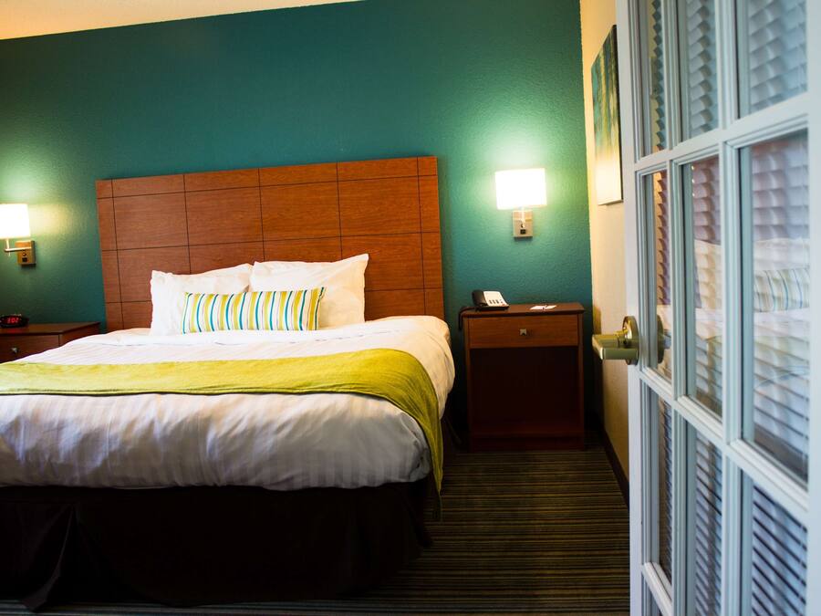 A hotel room with a large bed, two bedside tables, a nightstand, and a door with blinds.