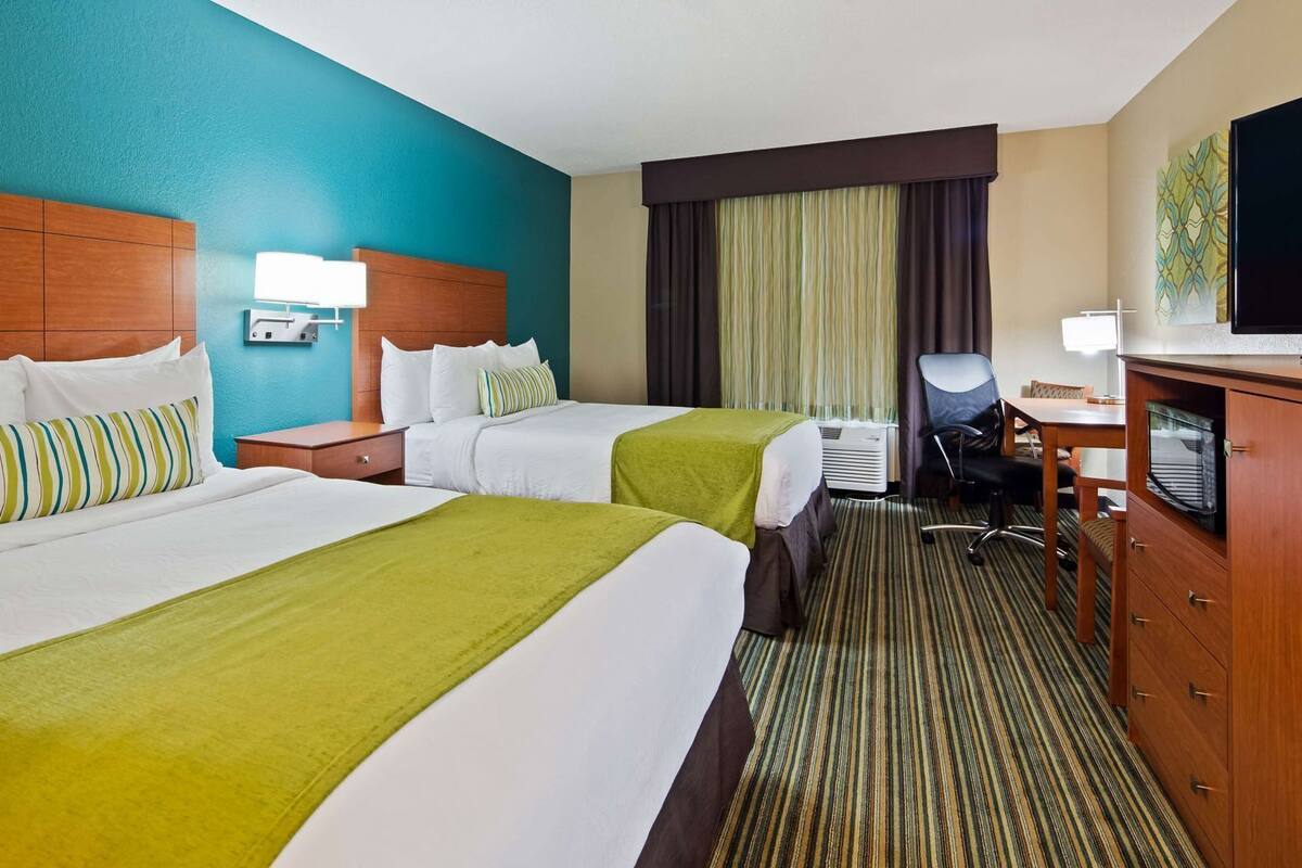 A hotel room with two beds, a desk, a chair, a television, and a minibar.