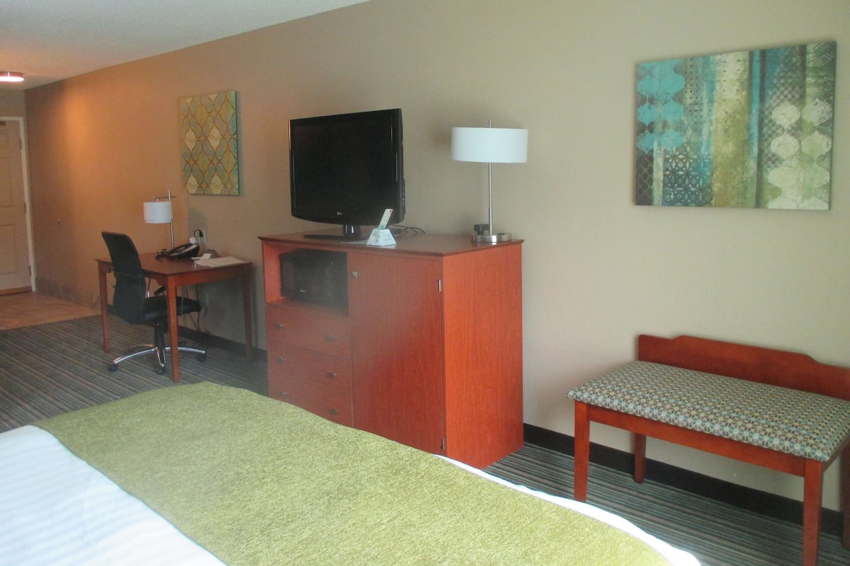 Una habitación de hotel con cama, escritorio con computadora, televisor, lámpara y silla.