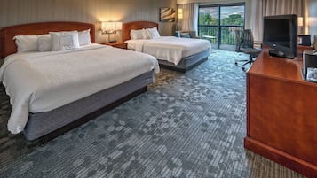 A hotel room with two beds, a desk with a television, and a balcony with a view.