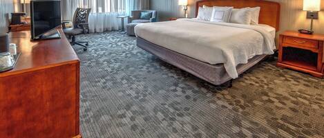A hotel room with a large bed, a desk with a TV, a chair, and a small table.