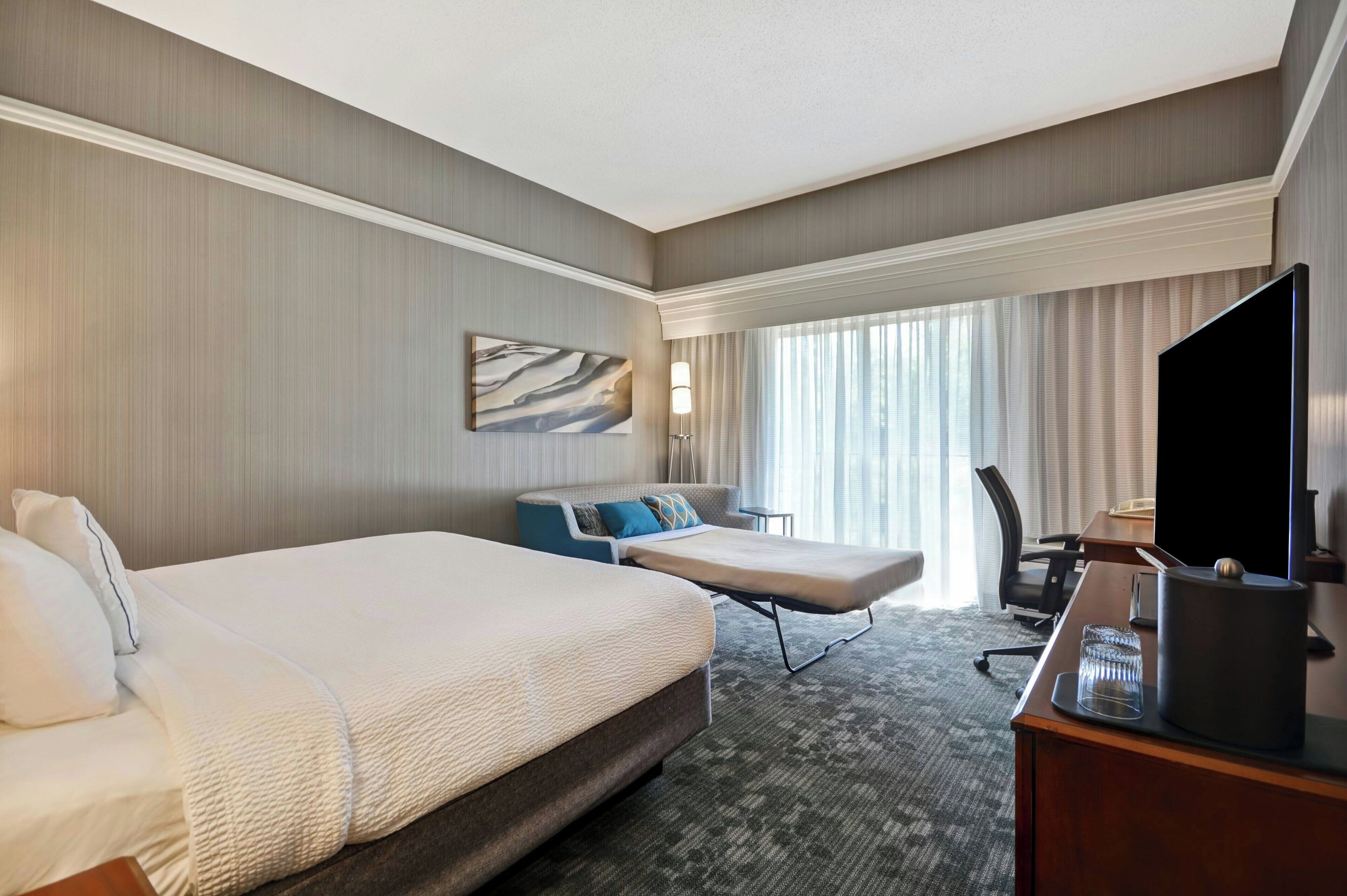Een hotelkamer met twee bedden, een bureau, een televisie en een groot raam met gordijnen.