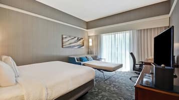 Een hotelkamer met twee bedden, een bureau, een televisie en een groot raam met gordijnen.