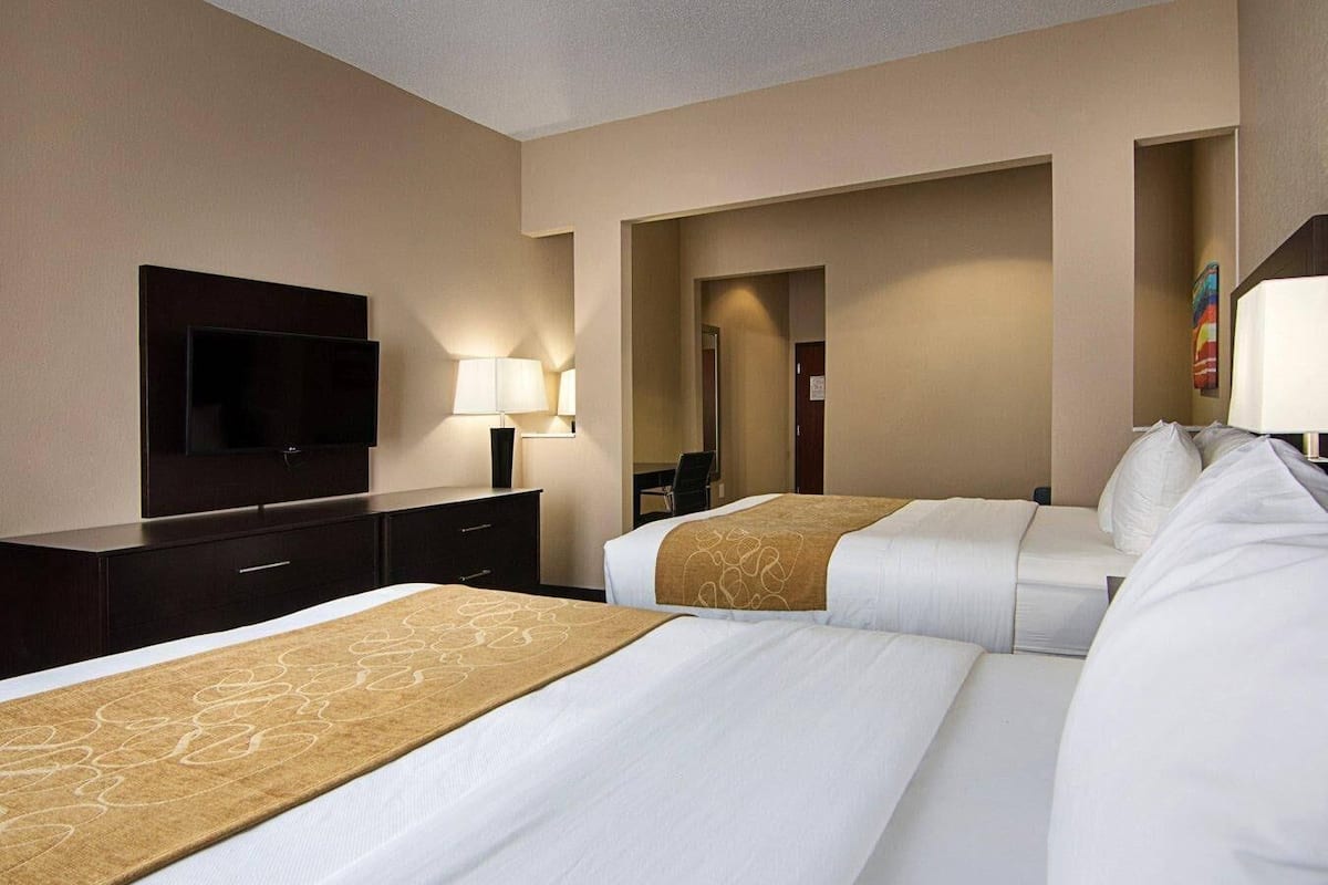 A hotel room with two beds, a TV, a desk, and a lamp.