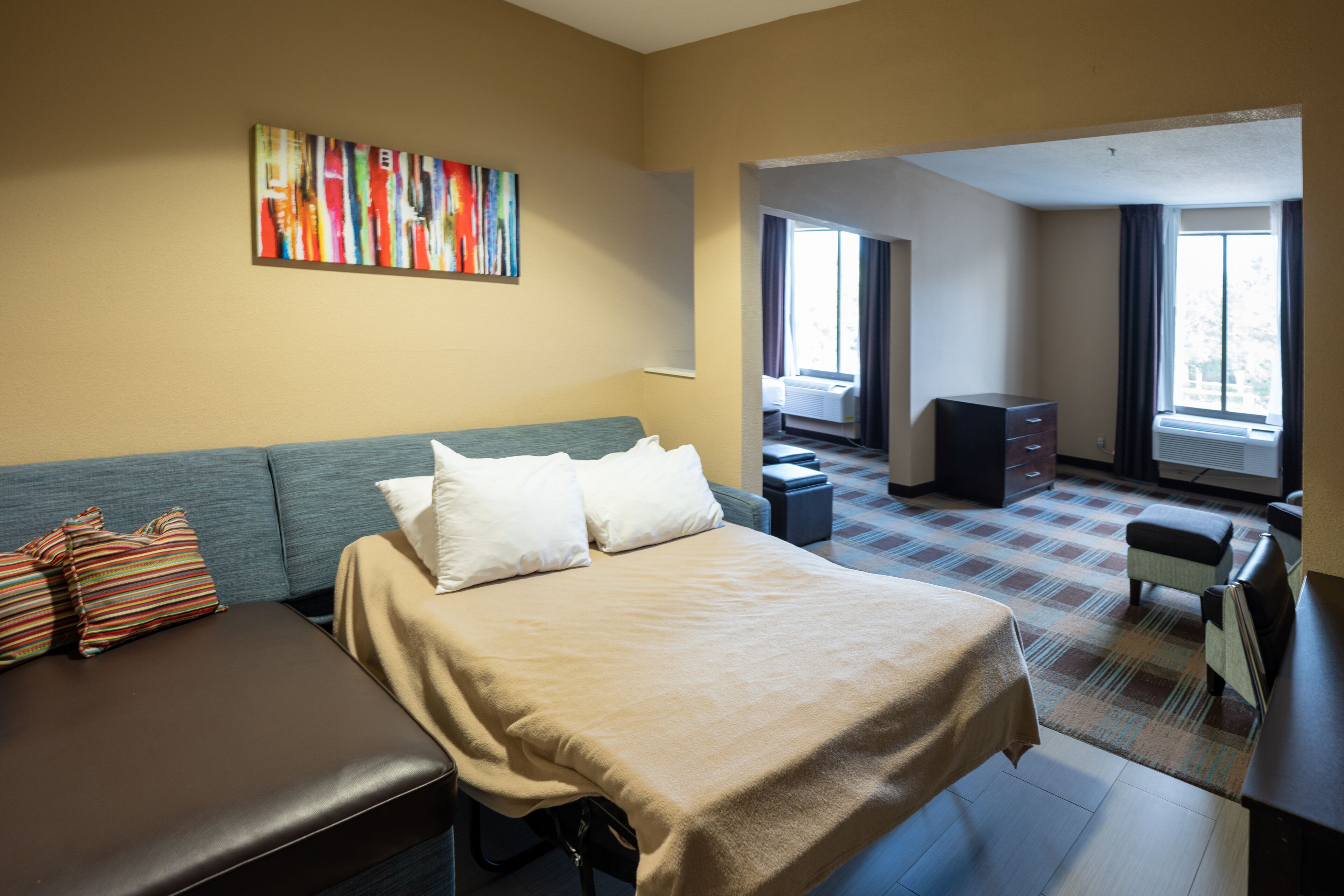 Habitació d'hotel amb un llit, un sofà, una taula de treball i una cadira. Hi ha un quadre a la paret i una finestra amb cortines.