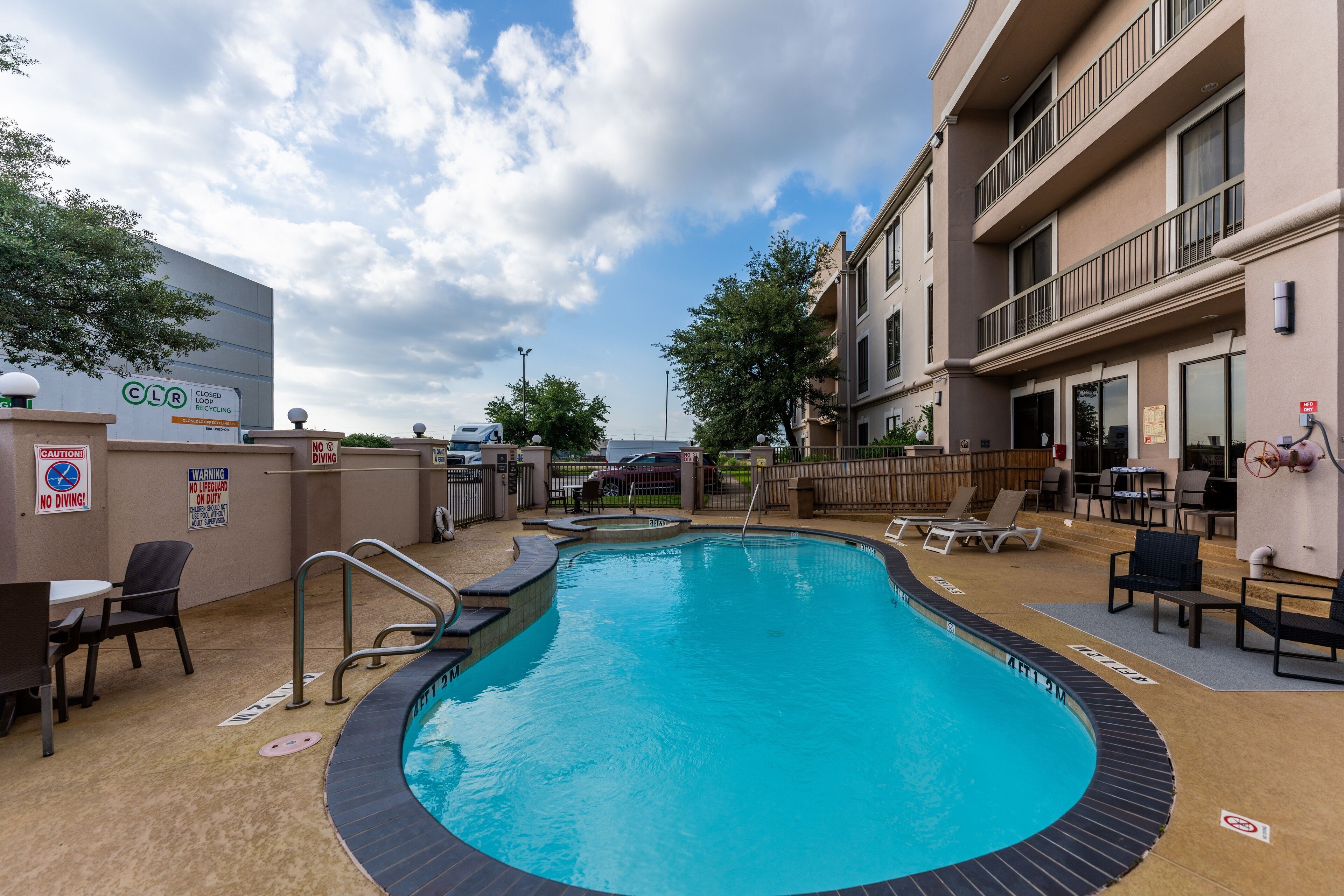An outdoor swimming pool with a poolside area, lounge chairs, and a building with balconies.